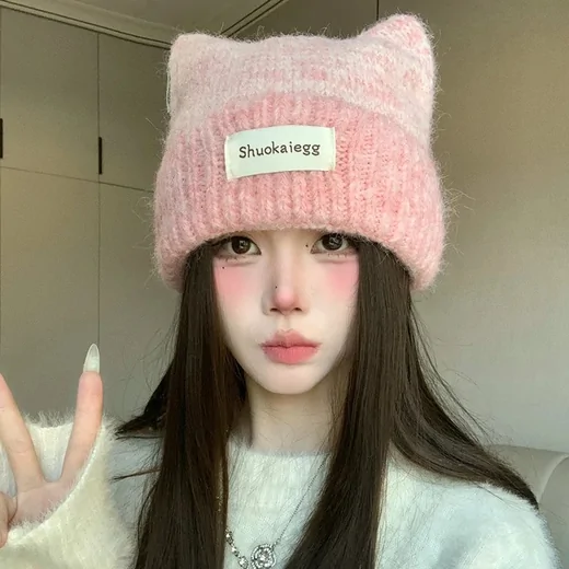 Young woman wearing a fluffy pink knit beanie with two pointed ears and a white label