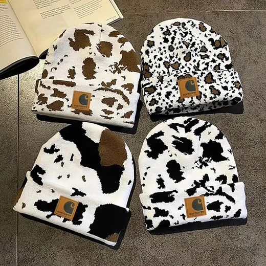 Four knitted beanies with cow-spot style patterns in brown, black and white