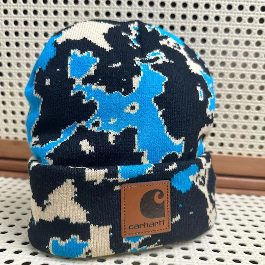 Knit beanie in a blue, black and cream camouflage pattern with a brown patch on the cuff