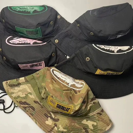 Pile of bucket hats in black and camouflage, some with chin cords and graphic patches
