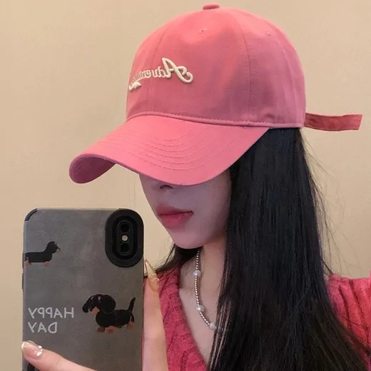 Woman wearing a pink baseball cap with white script stitching across the front