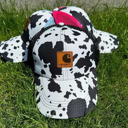 Black and white cow-print cap with a mesh back panel resting on grass