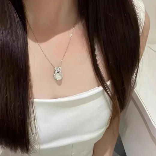 Woman in a white top wearing a fine chain with a small translucent white pendant