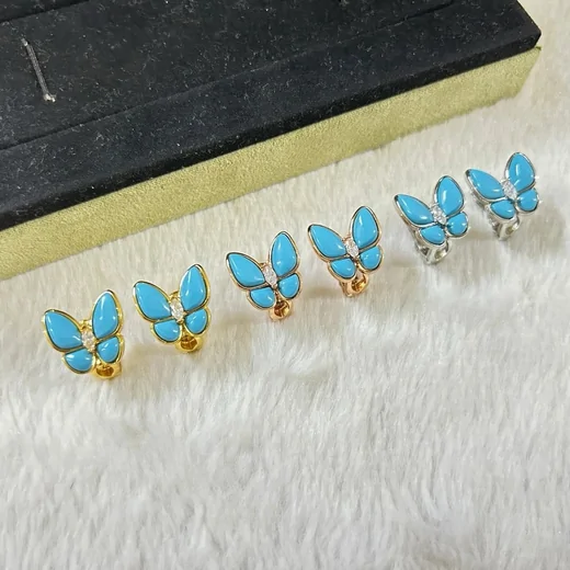 Turquoise butterfly stud earrings and small rings arranged on a dark box lid