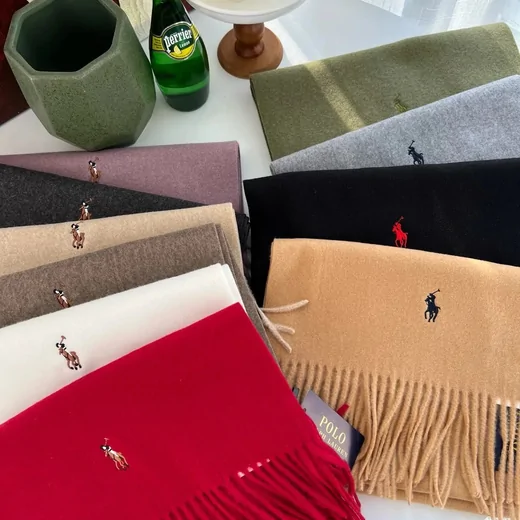 Folded fringed scarves in red, cream, camel and green next to a paper gift bag