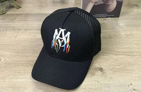 Black trucker cap with multicolour drip embroidery on a bookshelf