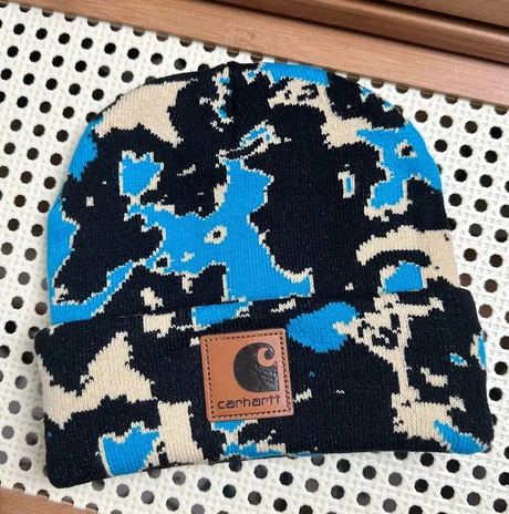 Blue, black and cream camouflage knit beanie with a brown patch on a dotted backdrop
