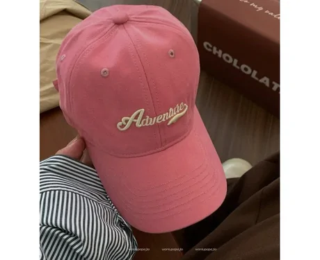 Pink baseball cap with white script embroidery on a desk