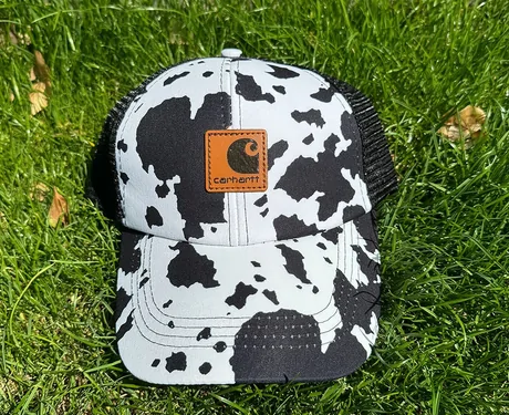 Cow-print trucker cap with a black mesh back on grass