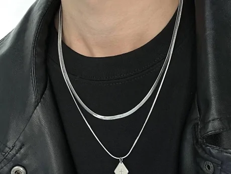 Man in a dark jacket wearing two layered silver-tone chains, one with a small pendant