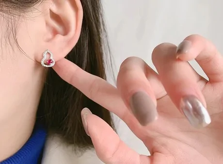 Hand touching an ear wearing a small silver-tone stud with a pink stone