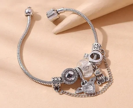 Silver snake-chain charm bracelet with beads and pendants on a beige surface