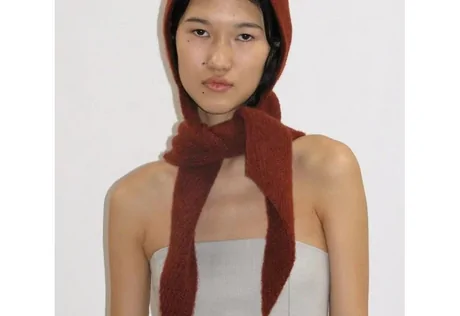 Model wearing a rust knitted hood with long ends tied at the neck