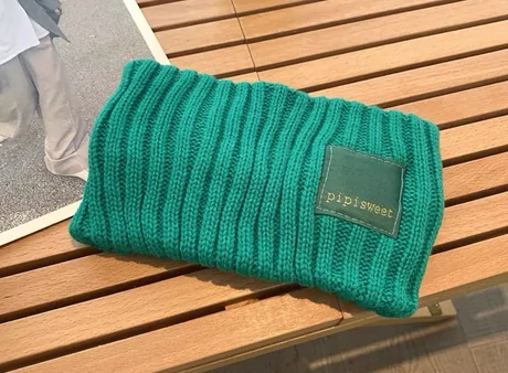 Green chunky rib beanie with a square woven label lying on a wooden bench