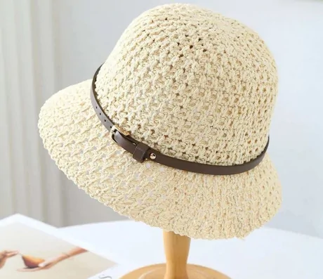 Cream open-crochet bucket hat with a brown band on a wooden hat stand